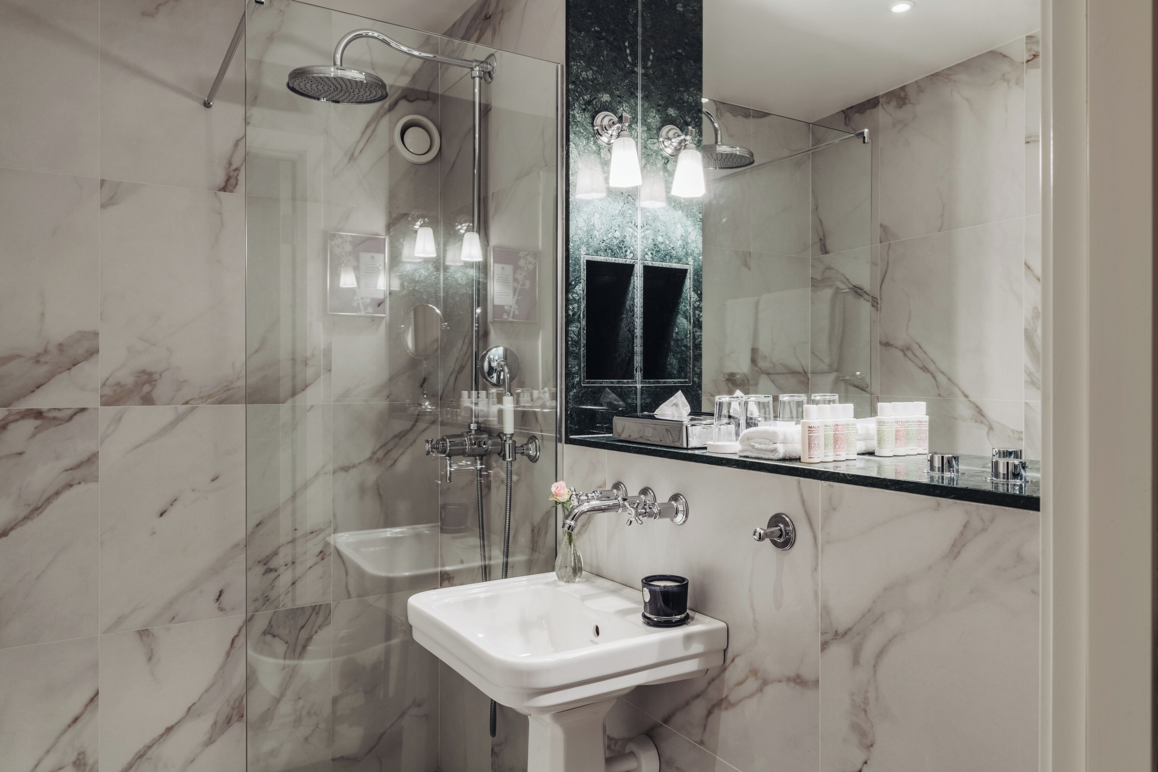 A modern bathroom with a glass-enclosed shower, a white sink, and a large mirror reflecting the room.