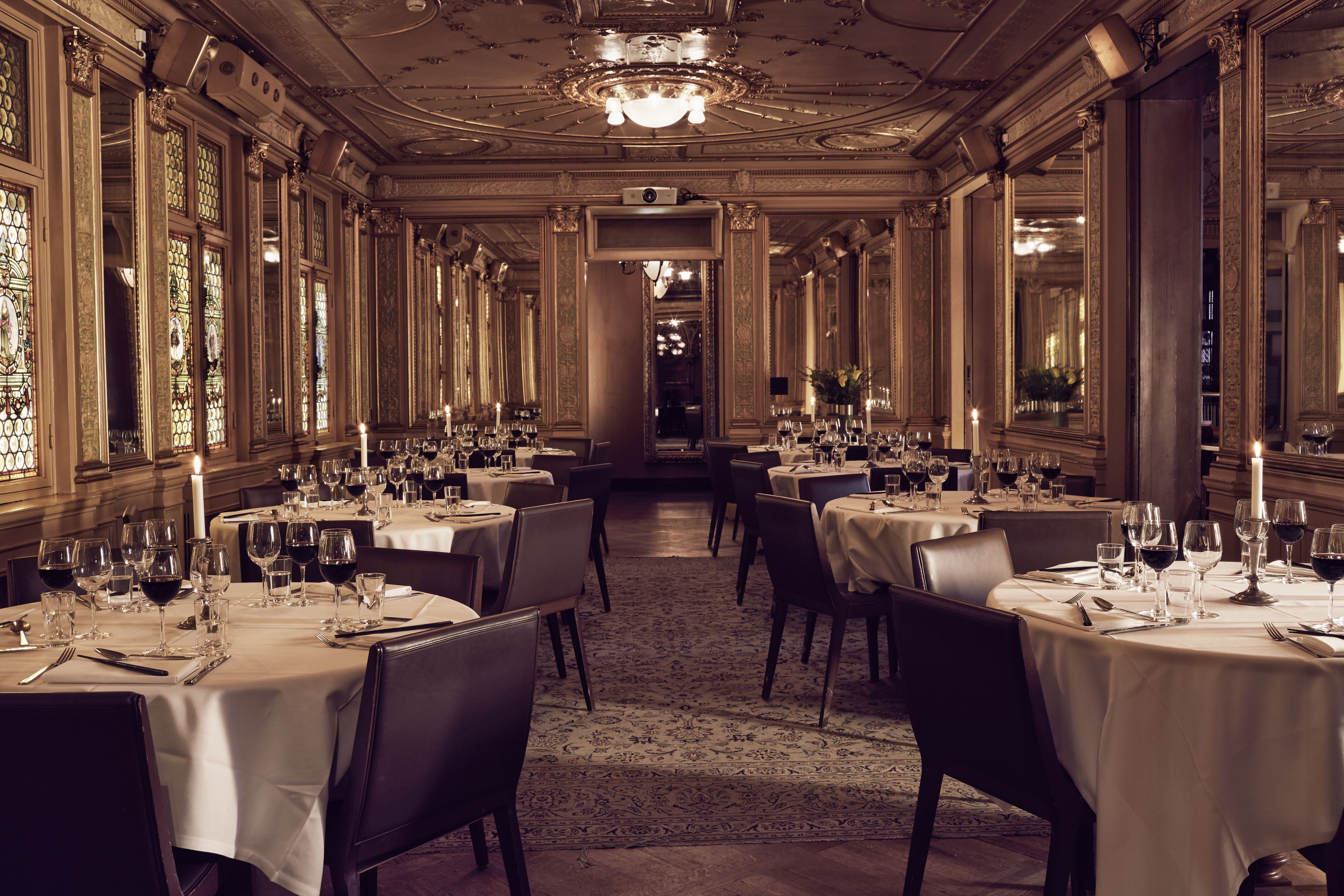 A formal dining room with multiple tables set for a meal, large windows, and ornate ceiling details.