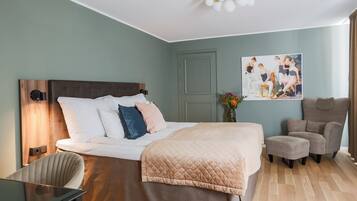Habitación de hotel con una cama grande, un escritorio, una silla, un sillón gris y un cuadro en la pared.