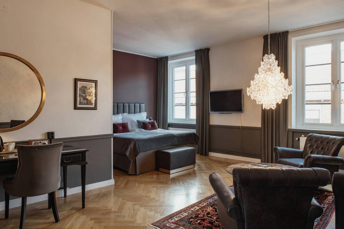 Una habitación de hotel moderna con una cama grande, un escritorio, una silla, un televisor y una araña.