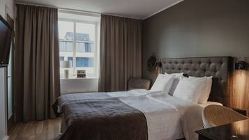 A hotel room with a large bed, a chair, a bedside table, a TV, and a window with curtains.