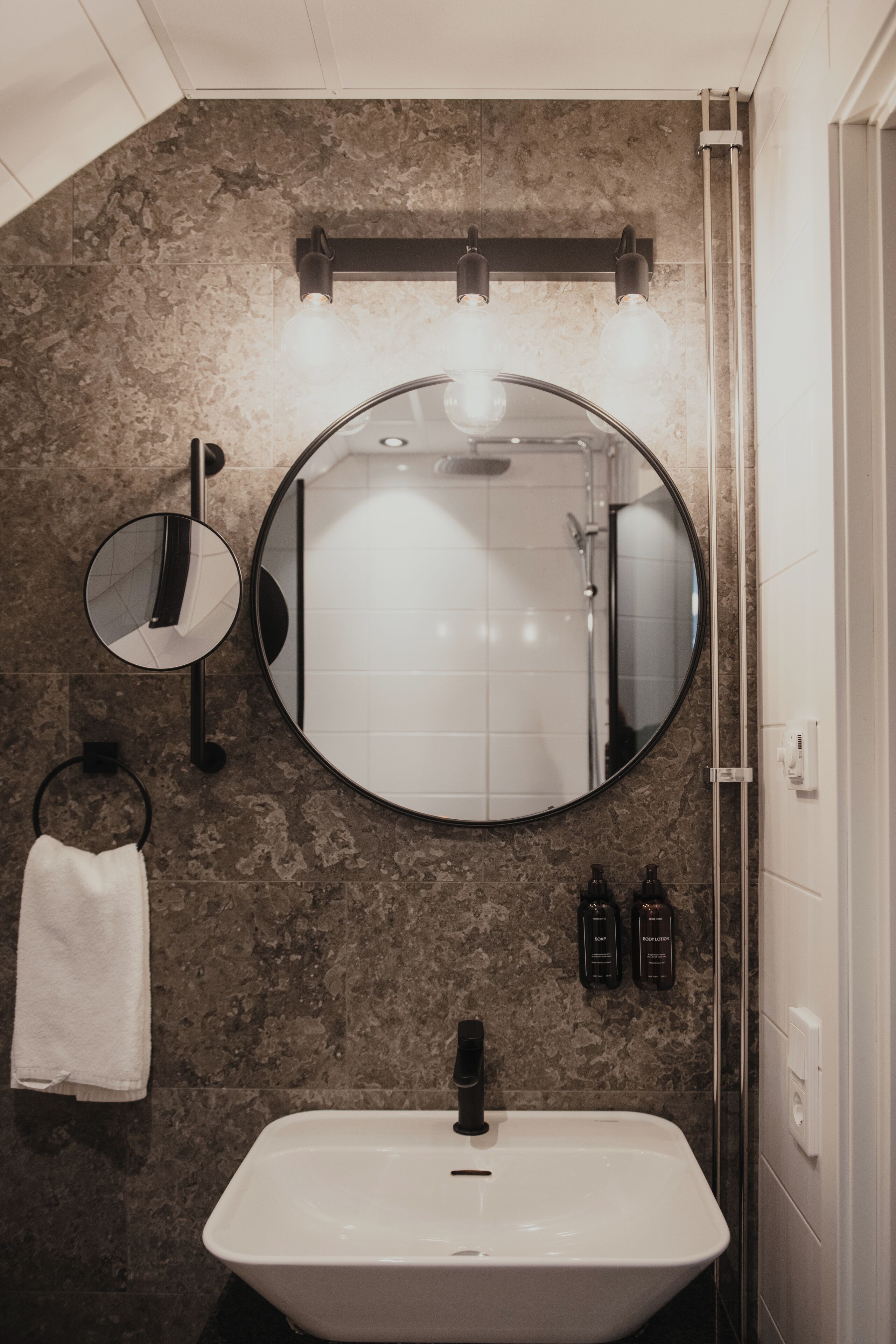 A bathroom with a round mirror, a rectangular mirror, a sink, and a towel rack.