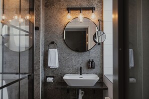 A modern bathroom with a round mirror, a white sink, and a towel rack.