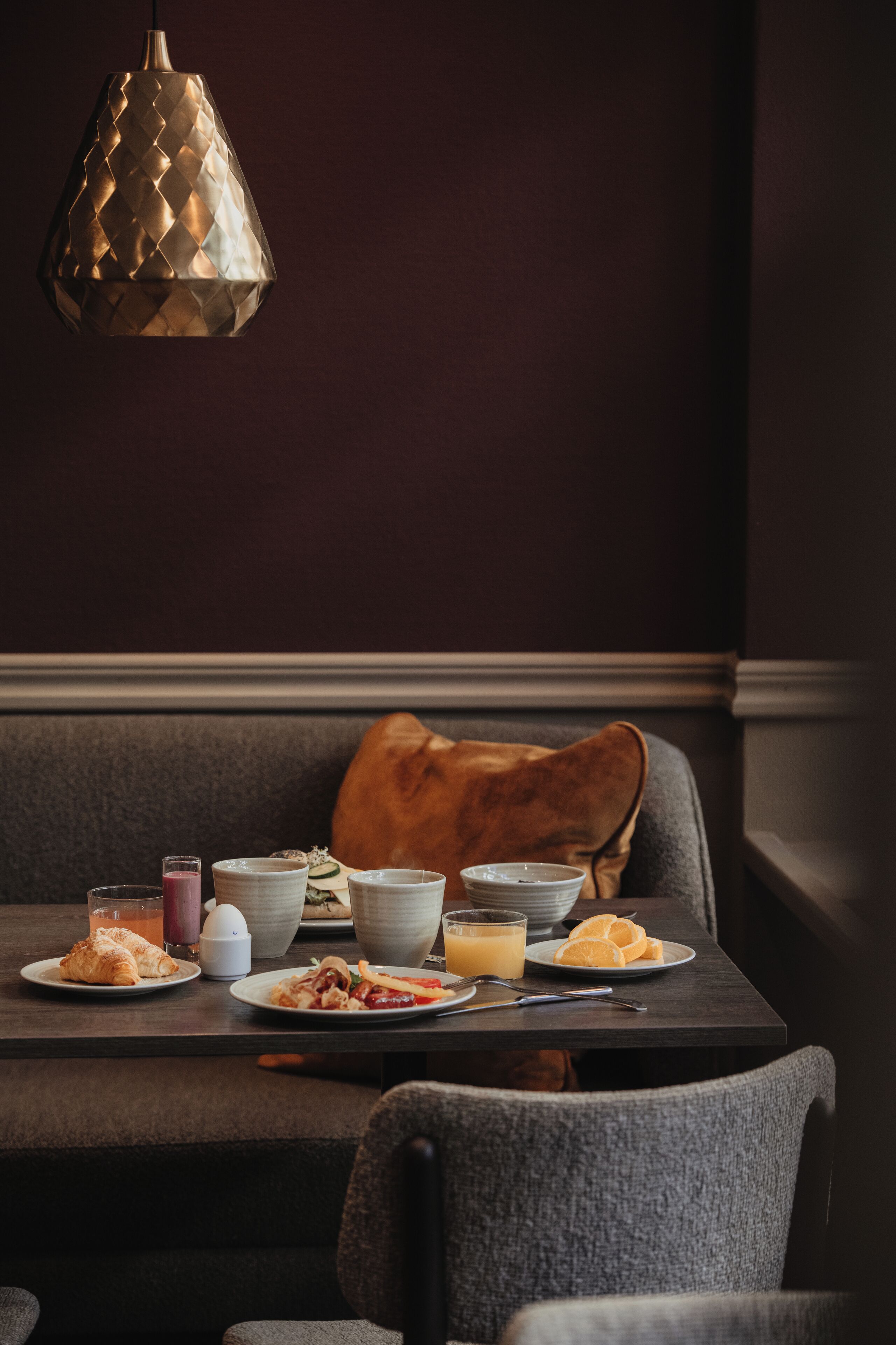 A dining table set with breakfast items, a brown leather bench, and a textured pendant light.