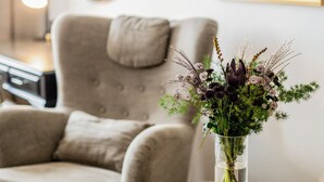 Una sala de estar con una mesa redonda, un sillón color beige y un jarrón con flores.