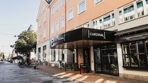 Un hotel con fachada moderna, un acceso cubierto y una zona de estar visible en el exterior.
