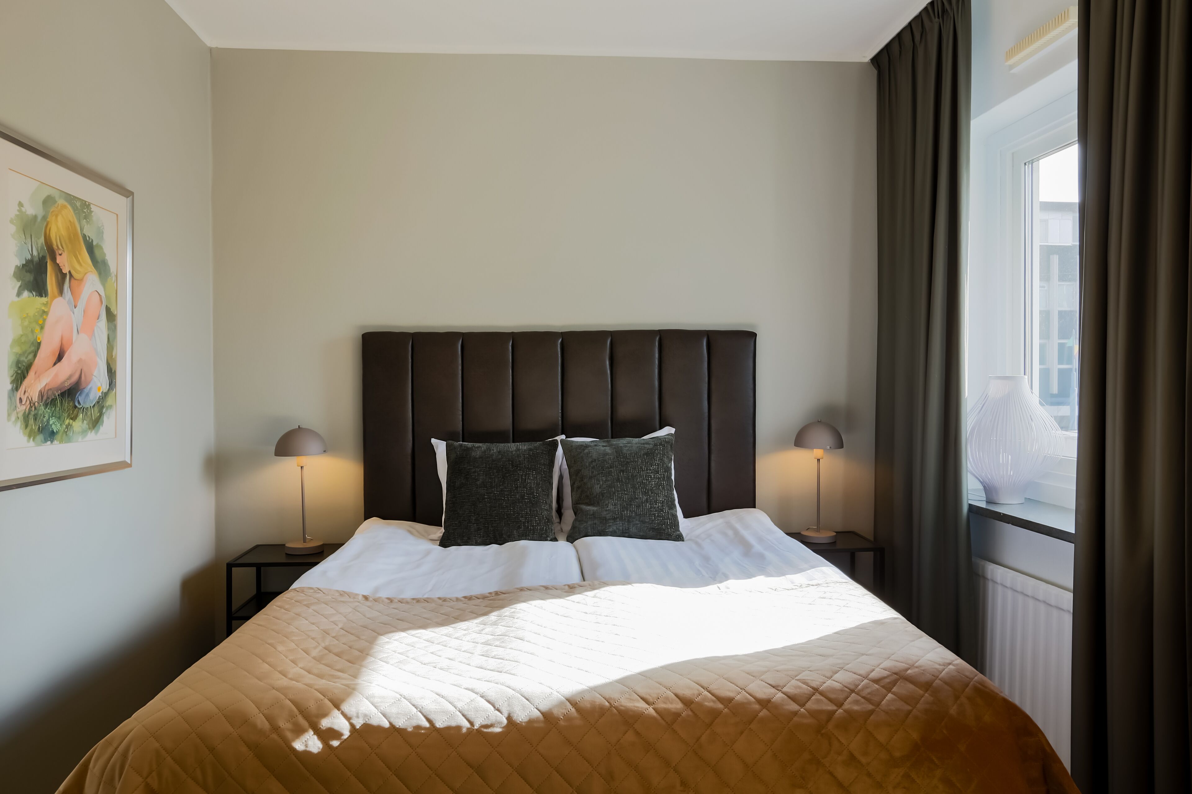 Une chambre d’hôtel avec un grand lit, deux lampes de chevet, une tête de lit et une fenêtre avec des rideaux.