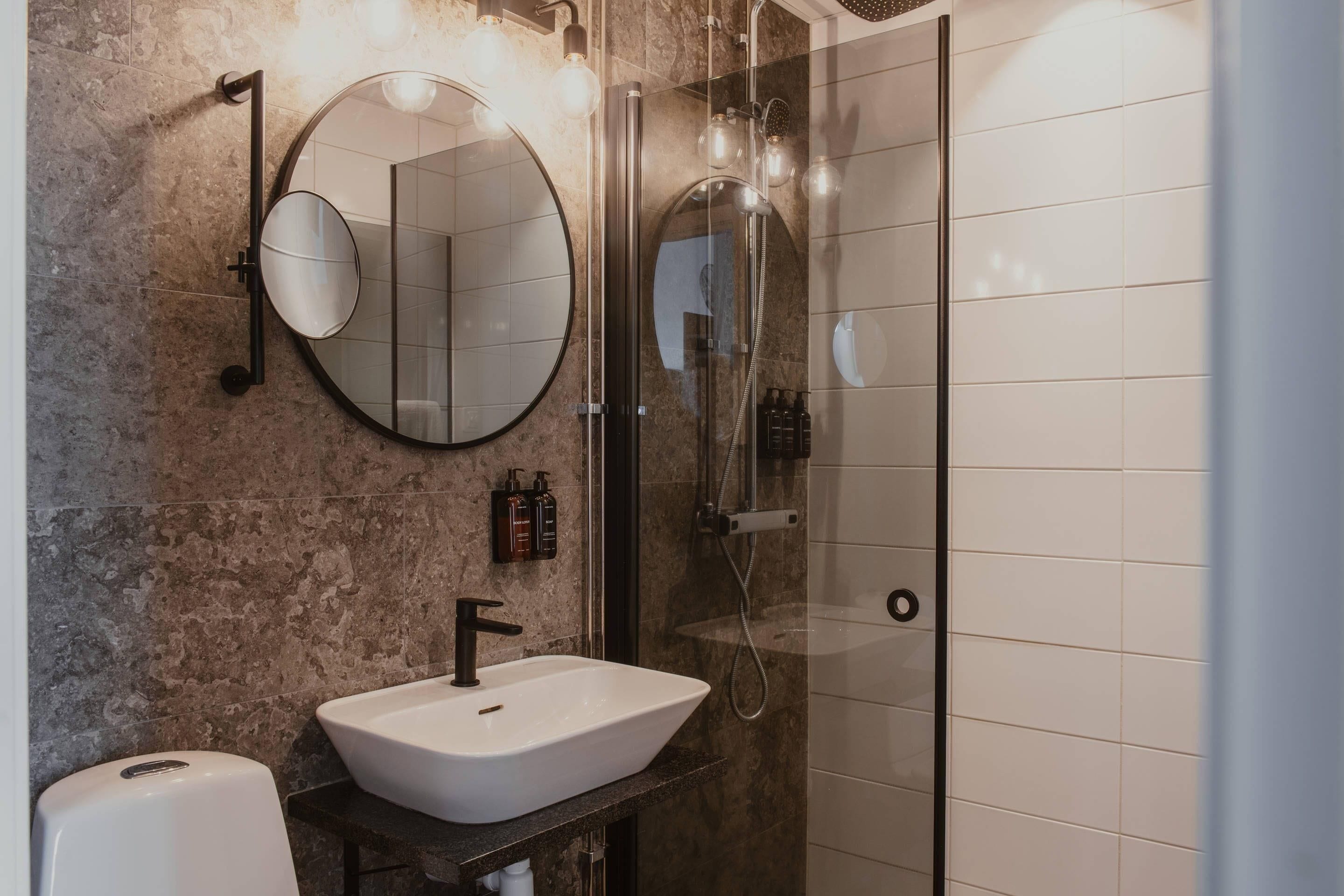 A modern bathroom with a round mirror, a white sink, and a glass-enclosed shower.
