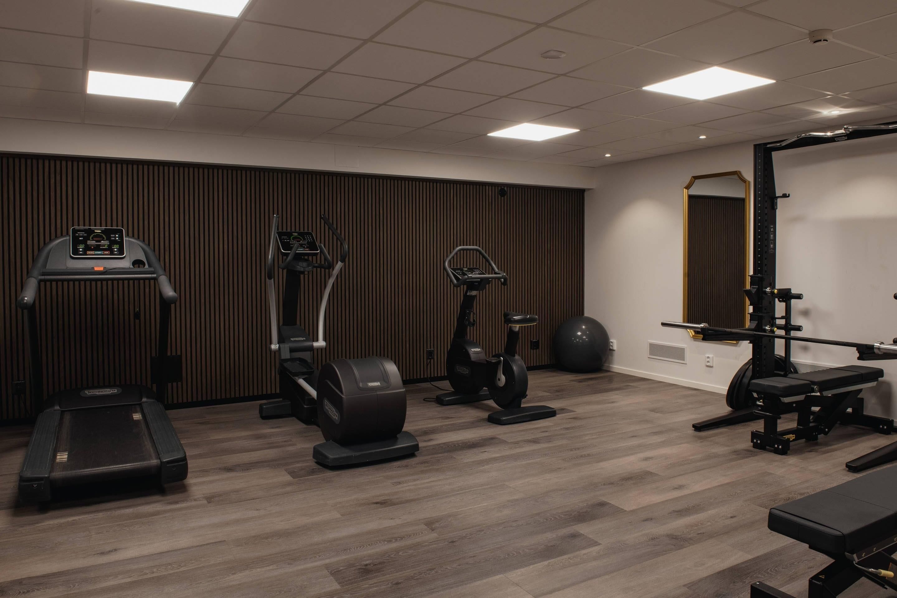 Een sportschool met loopbanden, elliptische trainers, een hometrainer en een gewichtbank.