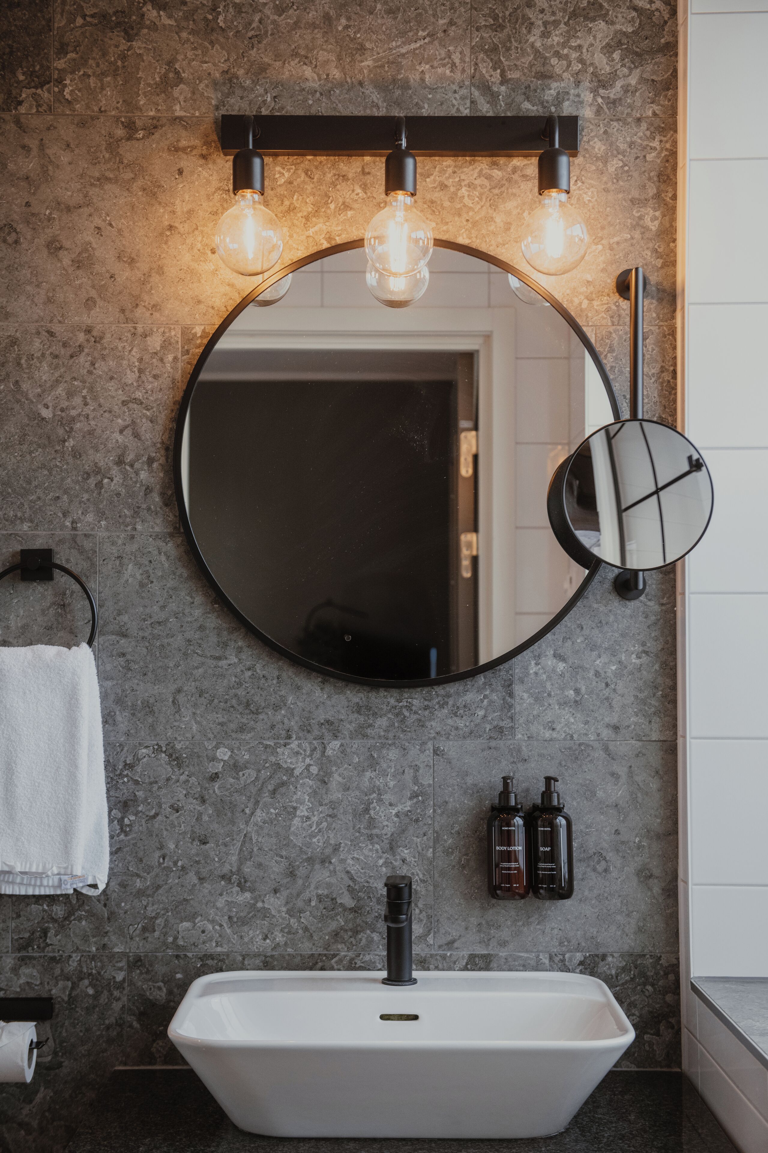 Een badkamer met een ronde spiegel, een witte wastafel en een handdoekhouder.