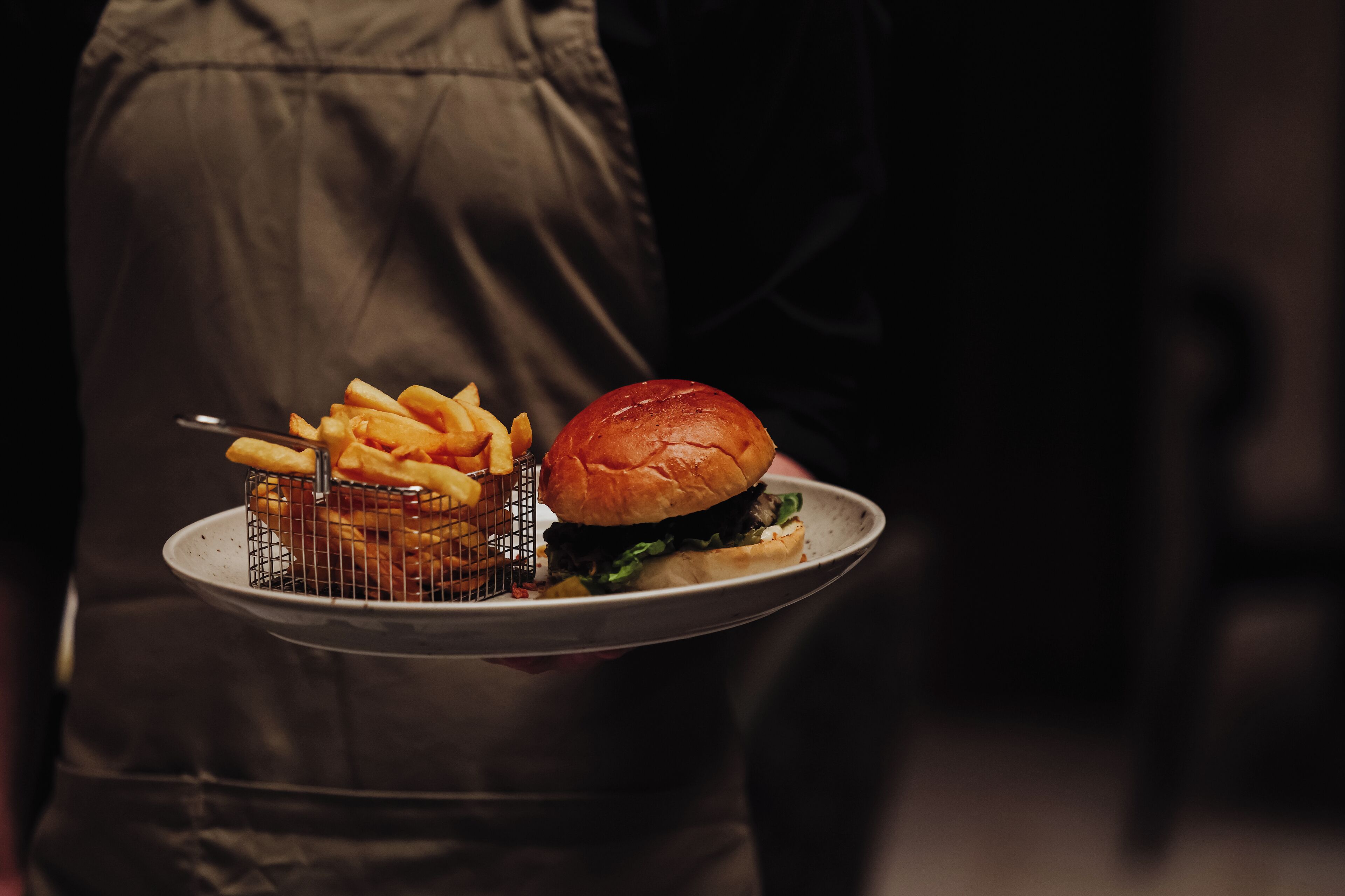 Eine Person hält ein Tablett mit einem Hamburger und Pommes.