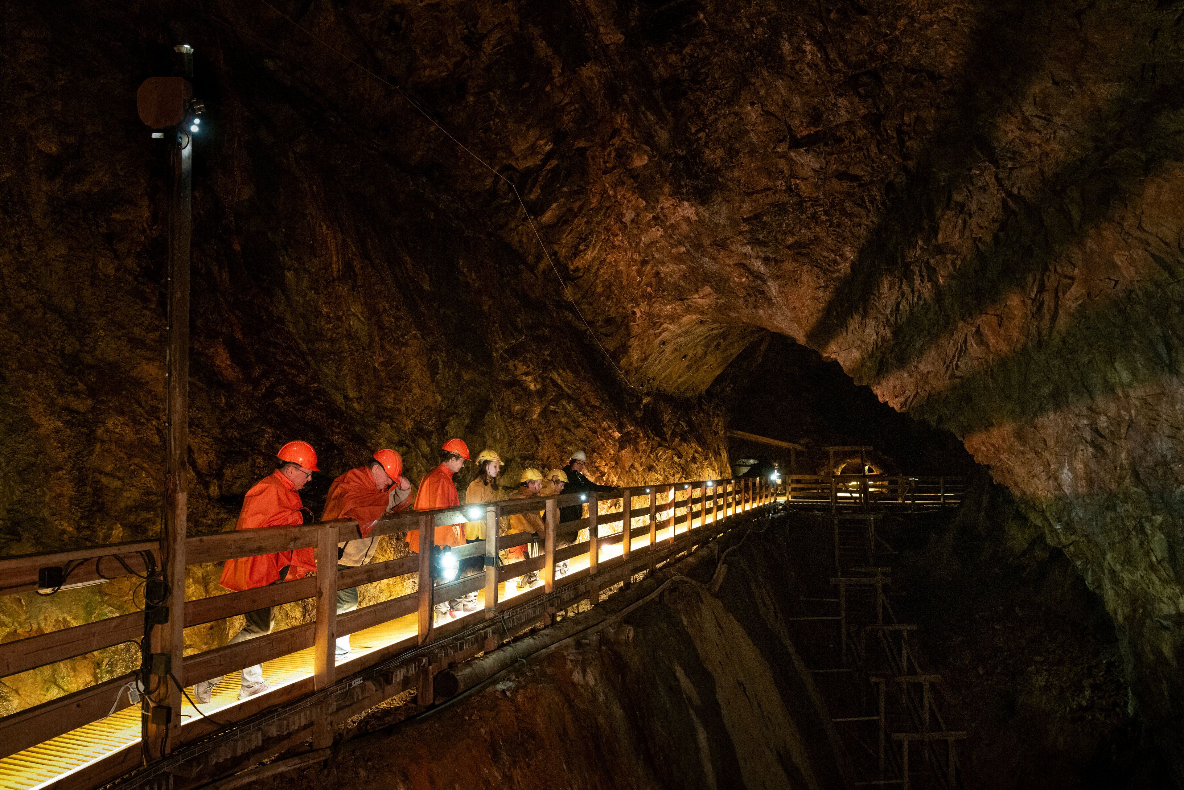 Un grupo de personas con equipo de seguridad naranja en una pasarela de madera dentro de una cueva.