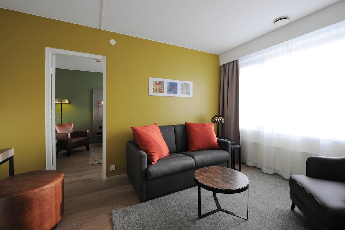 A living room with a sofa, two red cushions, a coffee table, and a view of a hallway.