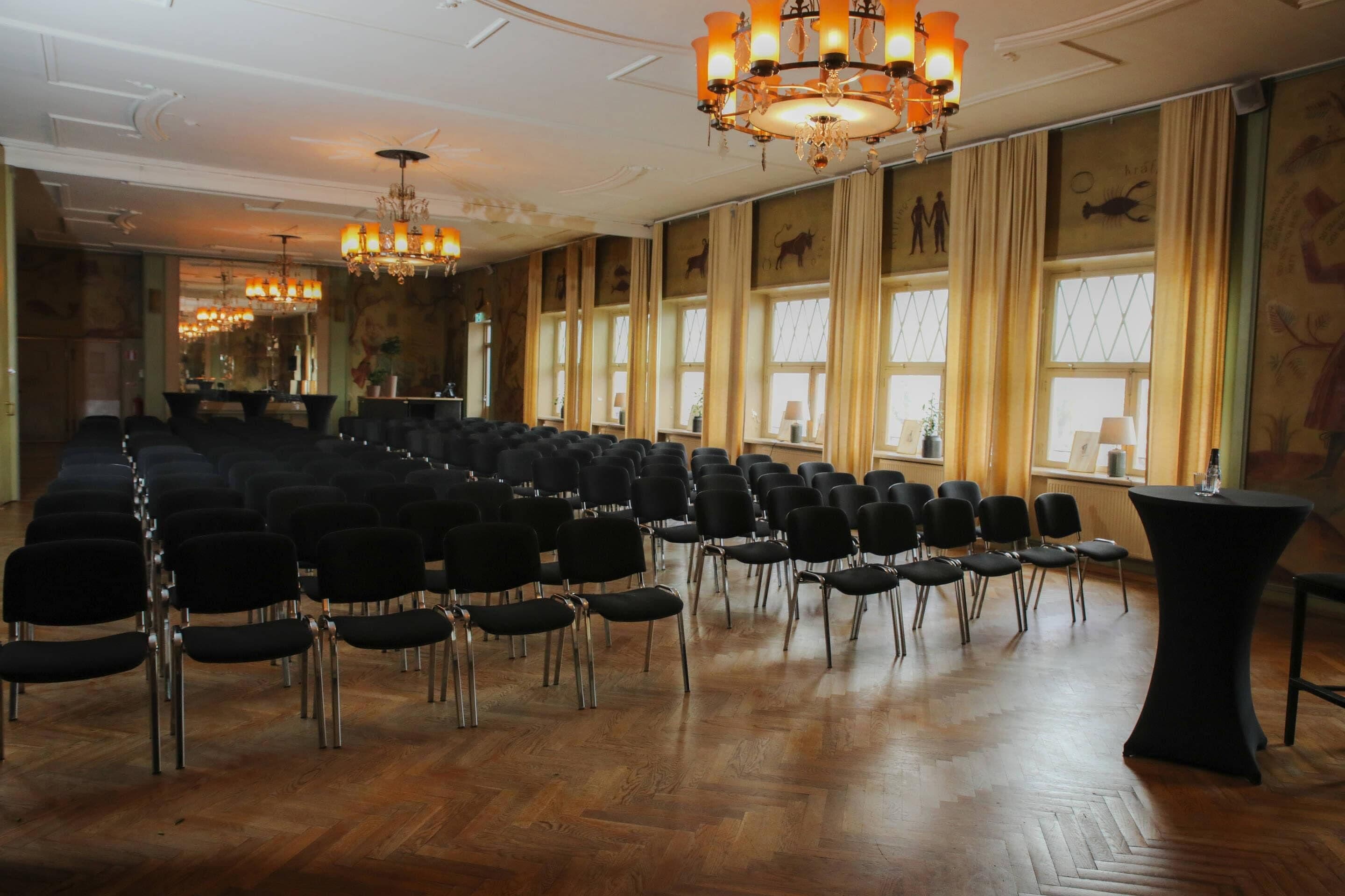 Un salón de conferencias con filas de sillas, un escenario y candelabros.