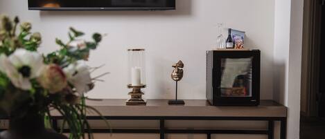 A modern living room with a flat-screen TV mounted on the wall, a wooden bench with decorative items, and a vase with flowers.