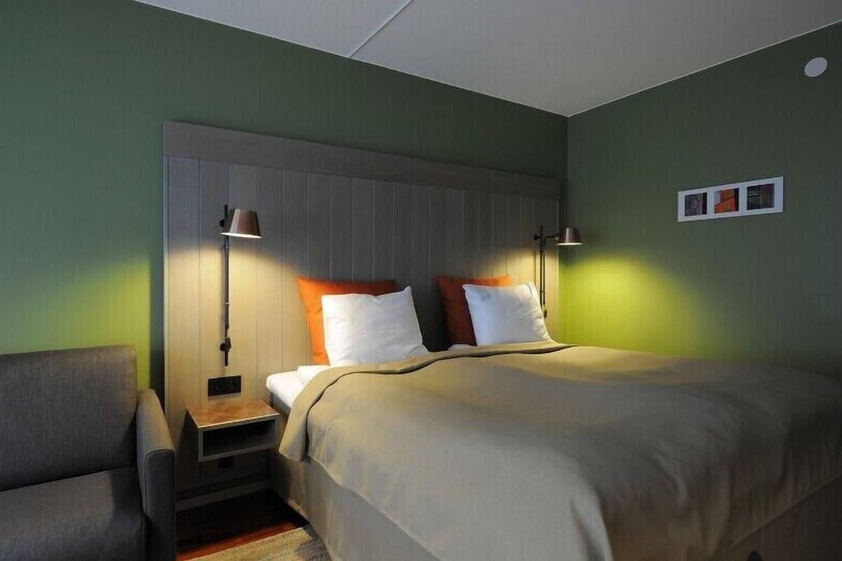 A hotel room with a bed, bedside tables, a chair, and a wall-mounted shelf.