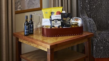 Una mesa de madera con una cesta de regalo que contiene varios artículos como botellas de vino, una copa y productos alimenticios.
