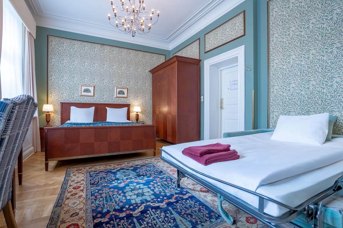 Una habitación de hotel con cama, una silla, armario, candelabro y pared con diseño.