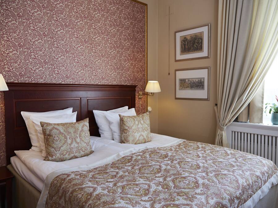 A neatly made bed with patterned bedding, a wooden headboard, and two wall-mounted lamps.
