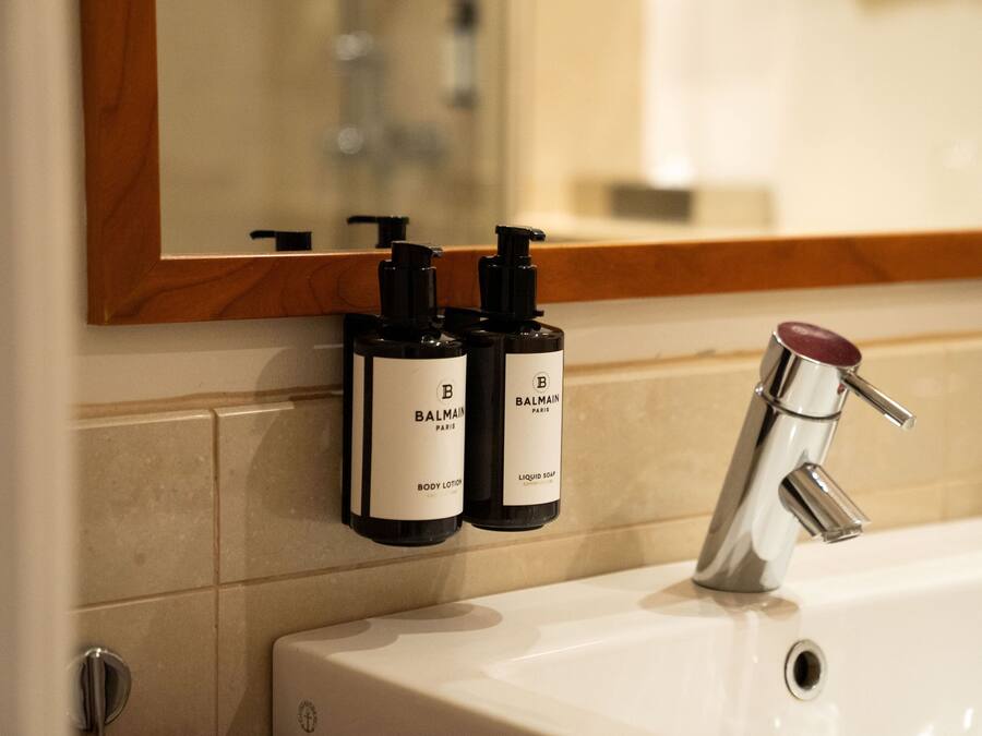 A bathroom with a white sink, a mirror with a wooden frame, and two bottles of Balmain body lotion and liquid soap.