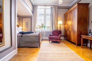 Un dormitorio con cama, una silla, armario, ventana y lámpara.