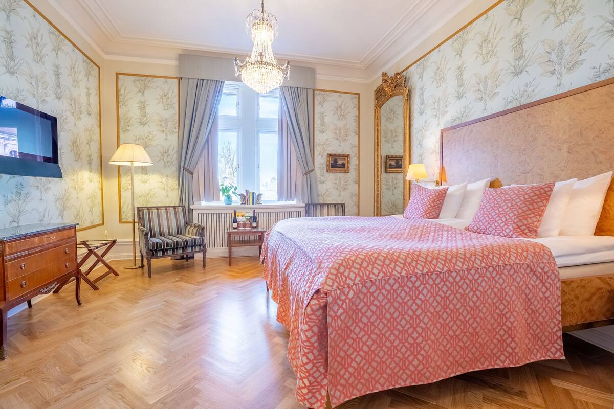 Una habitación de hotel con una cama grande, televisión, escritorio y una silla.