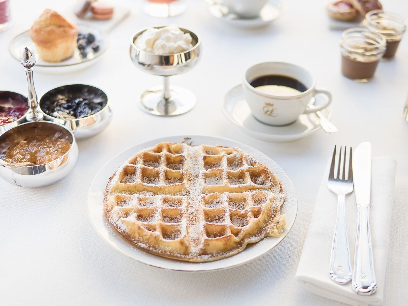 A breakfast setting with a waffle, coffee, and various pastries on a table.