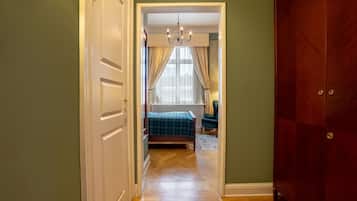 Um corredor que dá para um quarto com uma cama, um candelabro e um guarda-roupa.