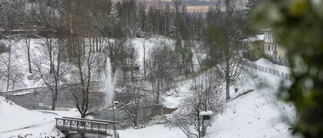 Un paisaje nevado con un puente, una cascada pequeña y un edificio al fondo.