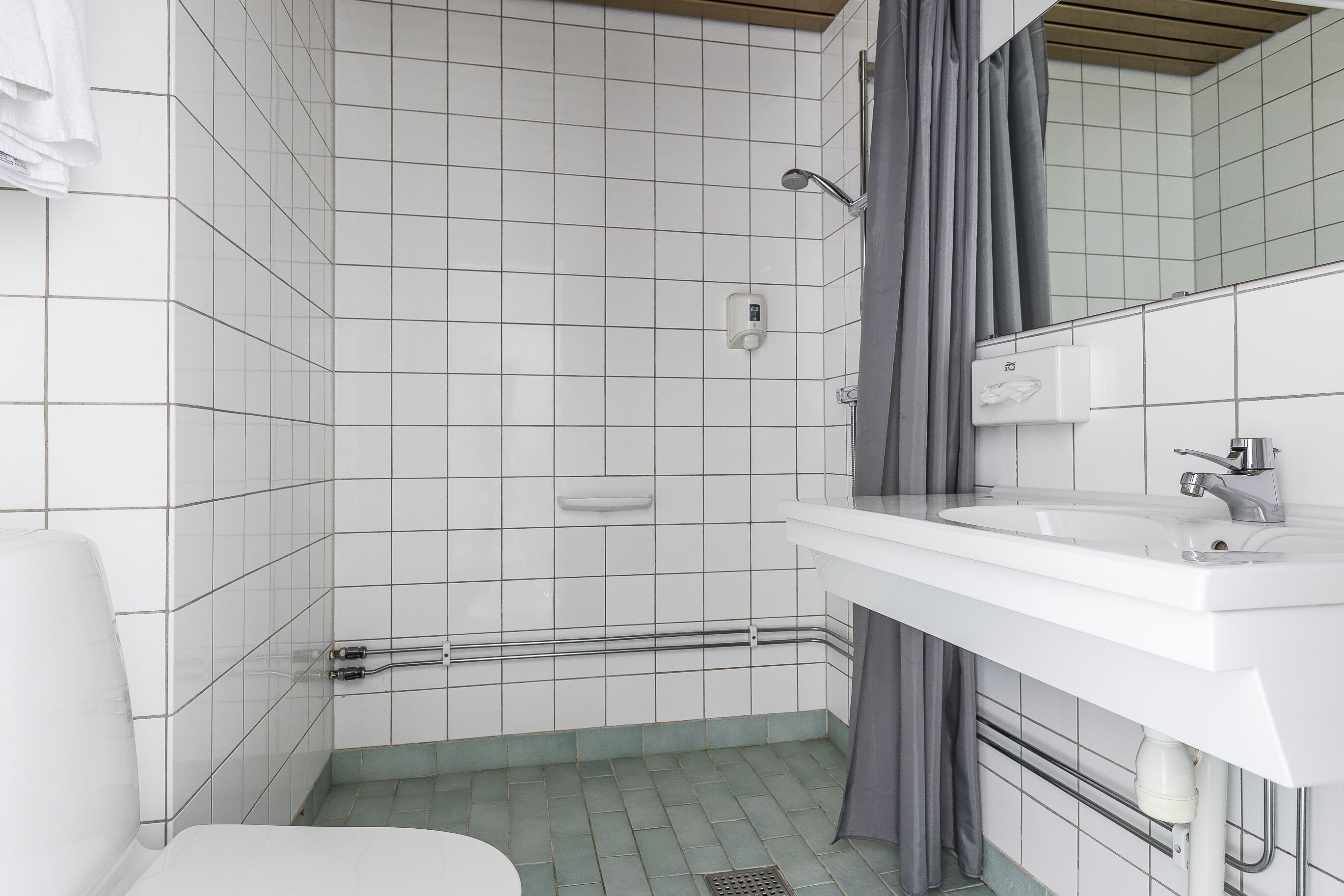 A bathroom with white tiled walls, a white sink, and a shower area.