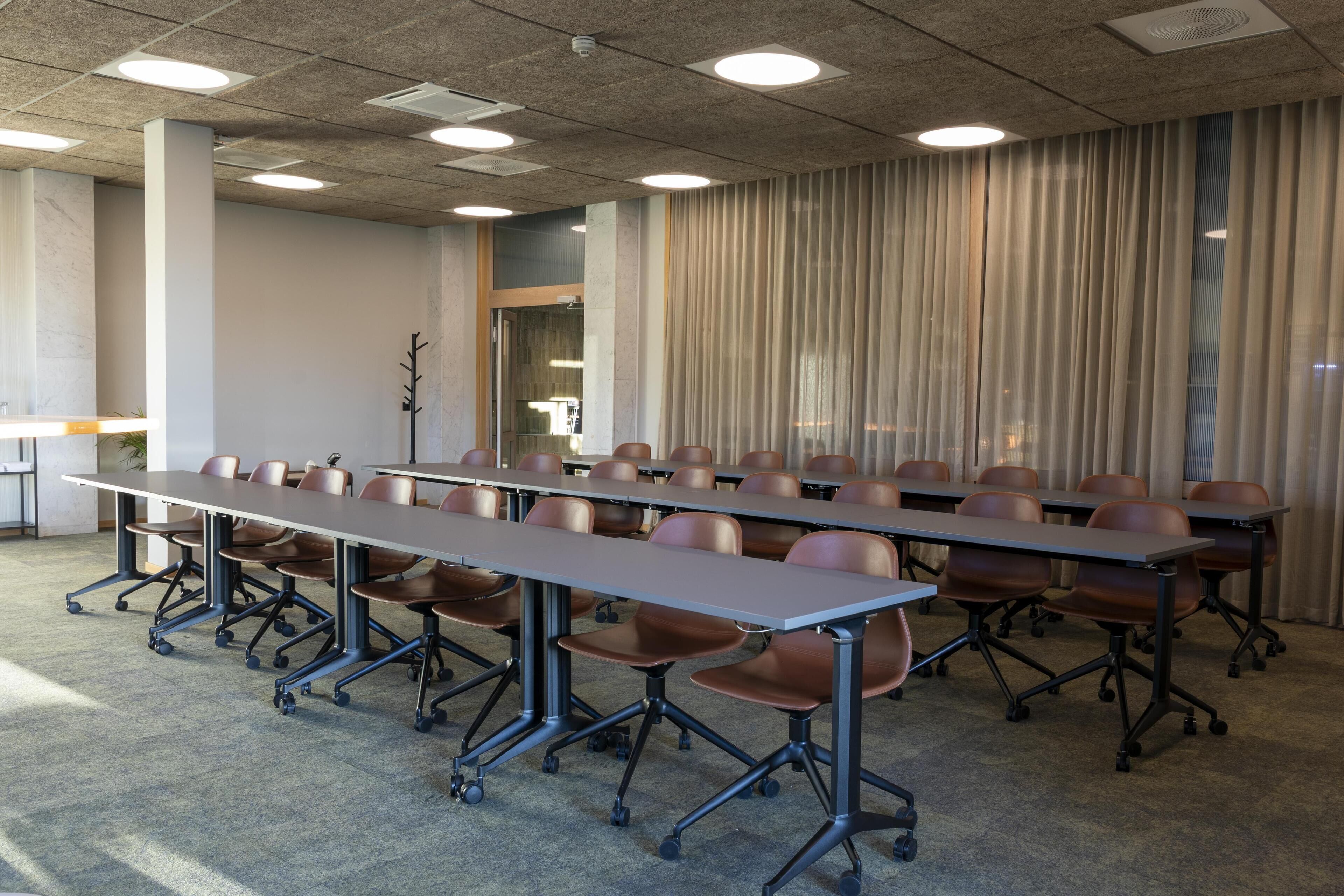 A conference room with long tables and chairs, a carpeted floor, and a ceiling with recessed lighting.