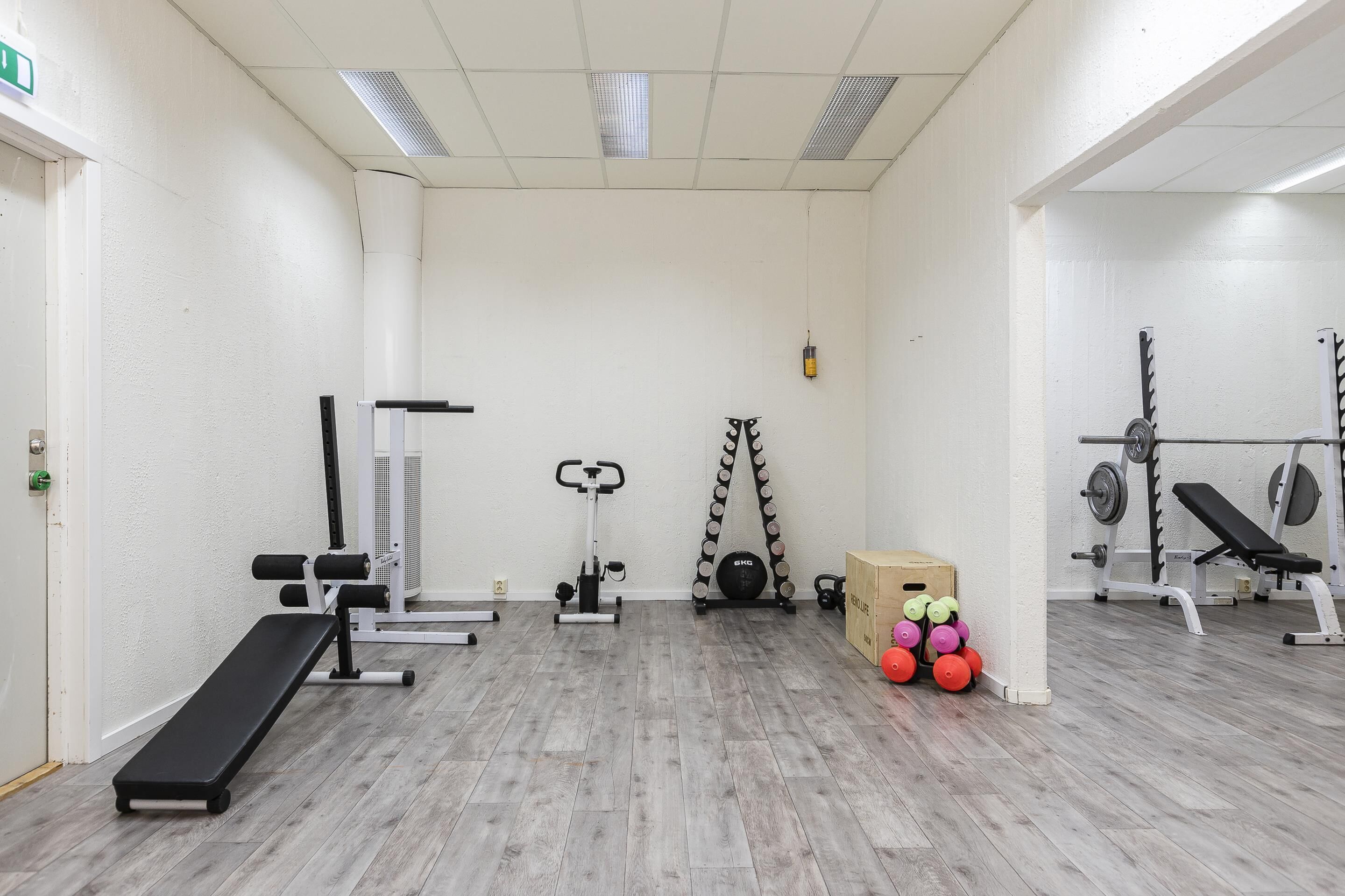 A gym with exercise equipment, a bench, and a wall-mounted rack with weights.