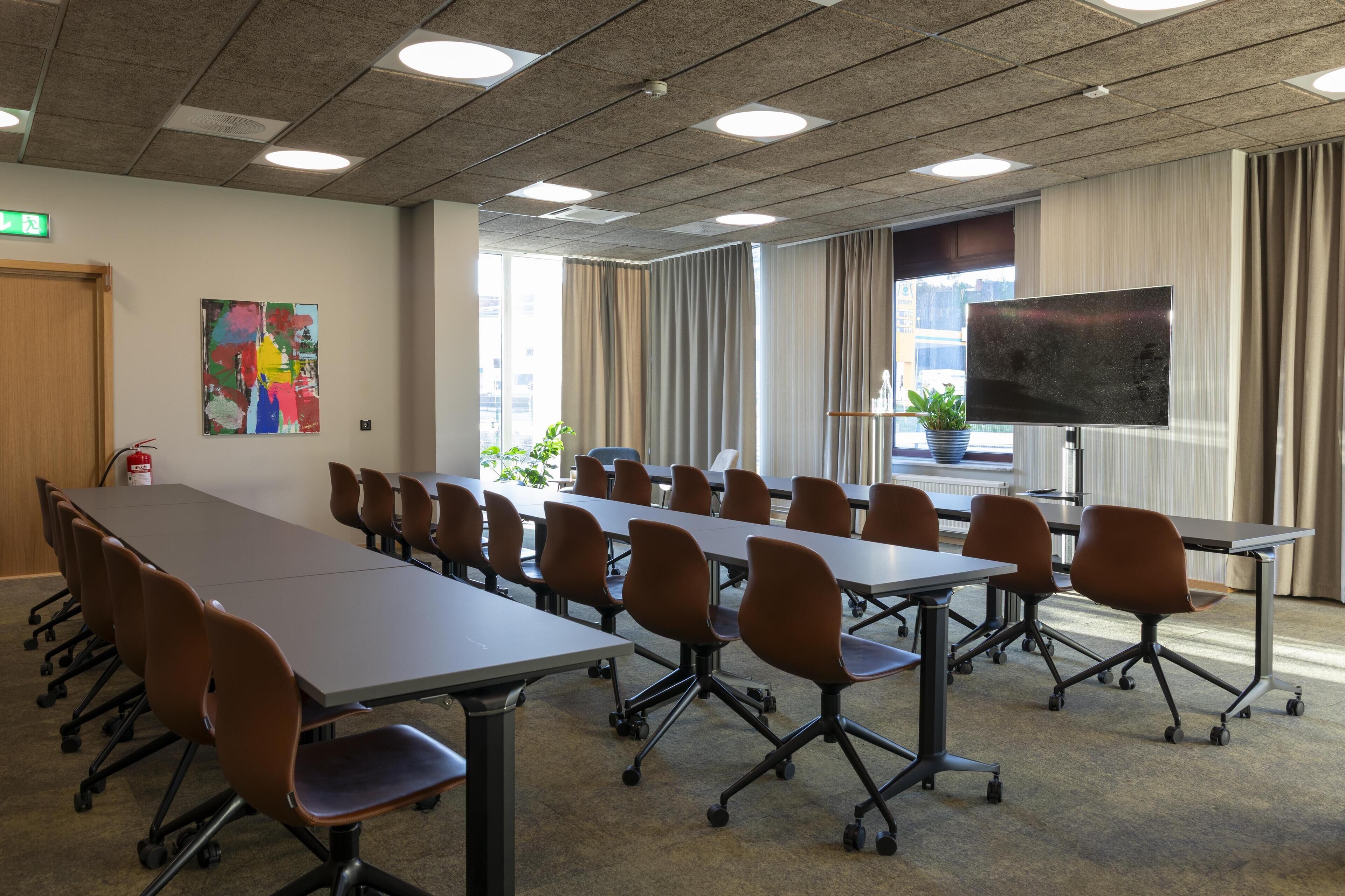 A conference room with a long table, multiple chairs, a flat-screen TV, and a large window with curtains.