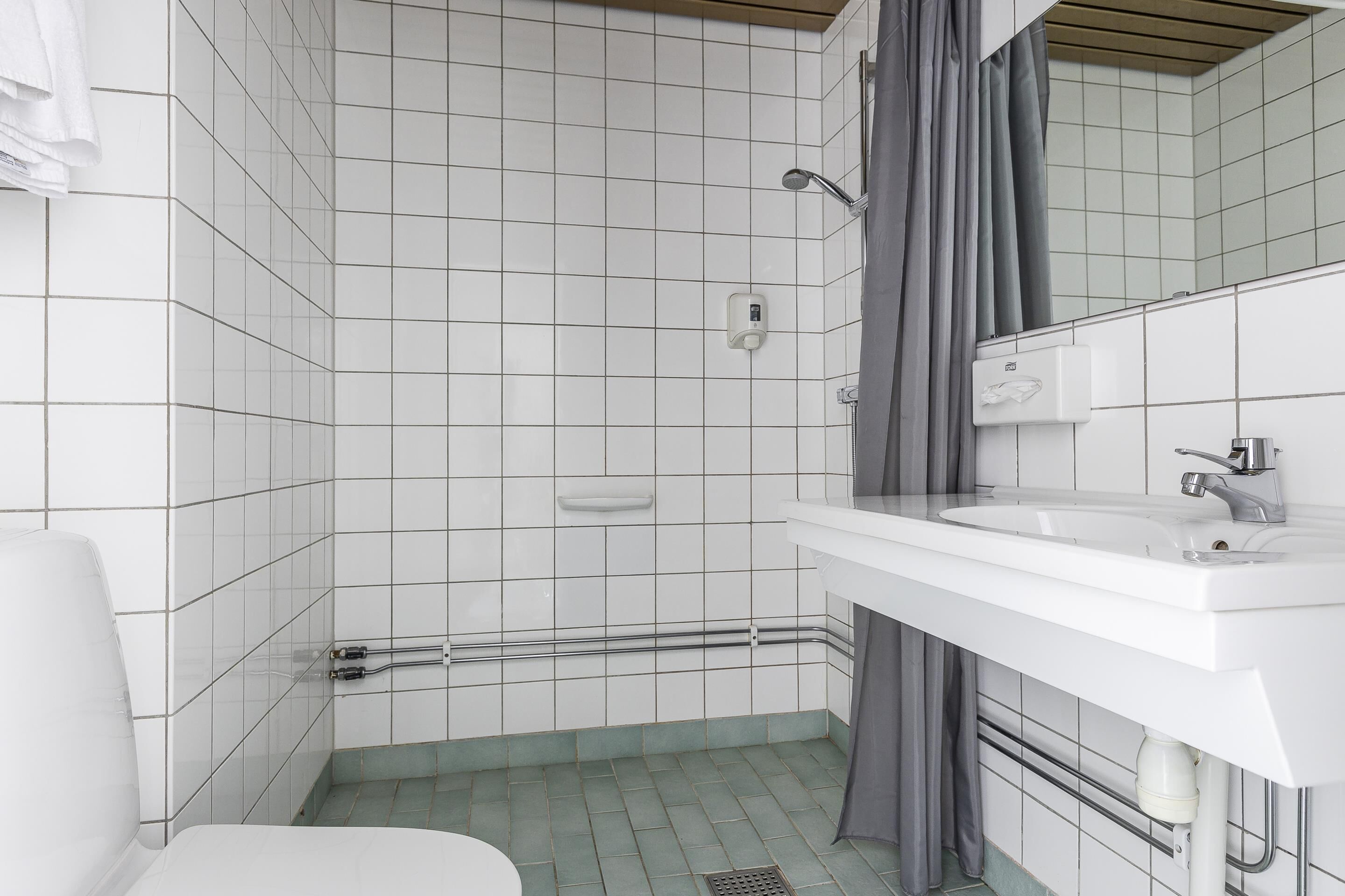 A bathroom with white tiled walls, a white sink, and a shower area.