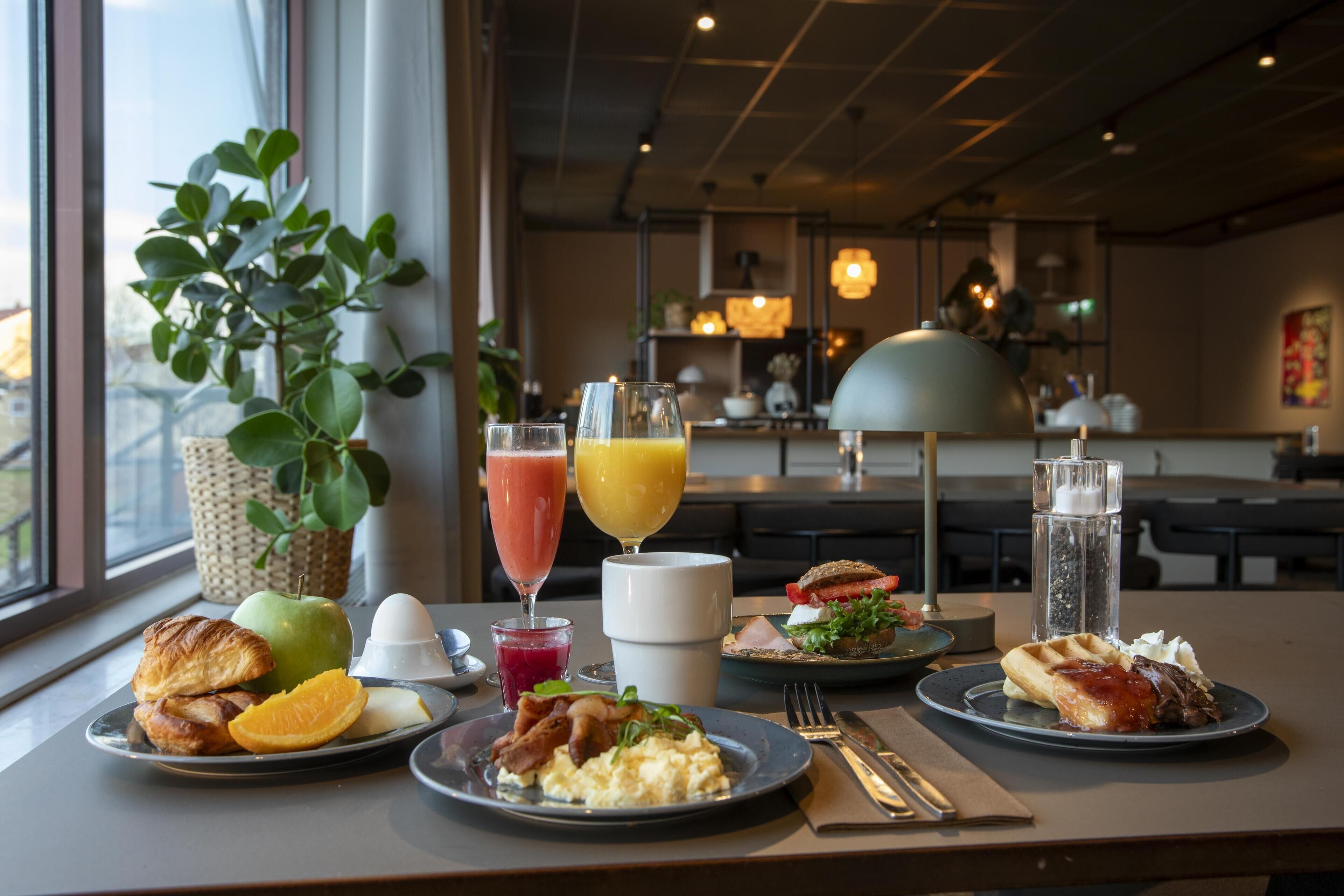 Et morgenbord med forskellige retter, drikkevarer og en plante.