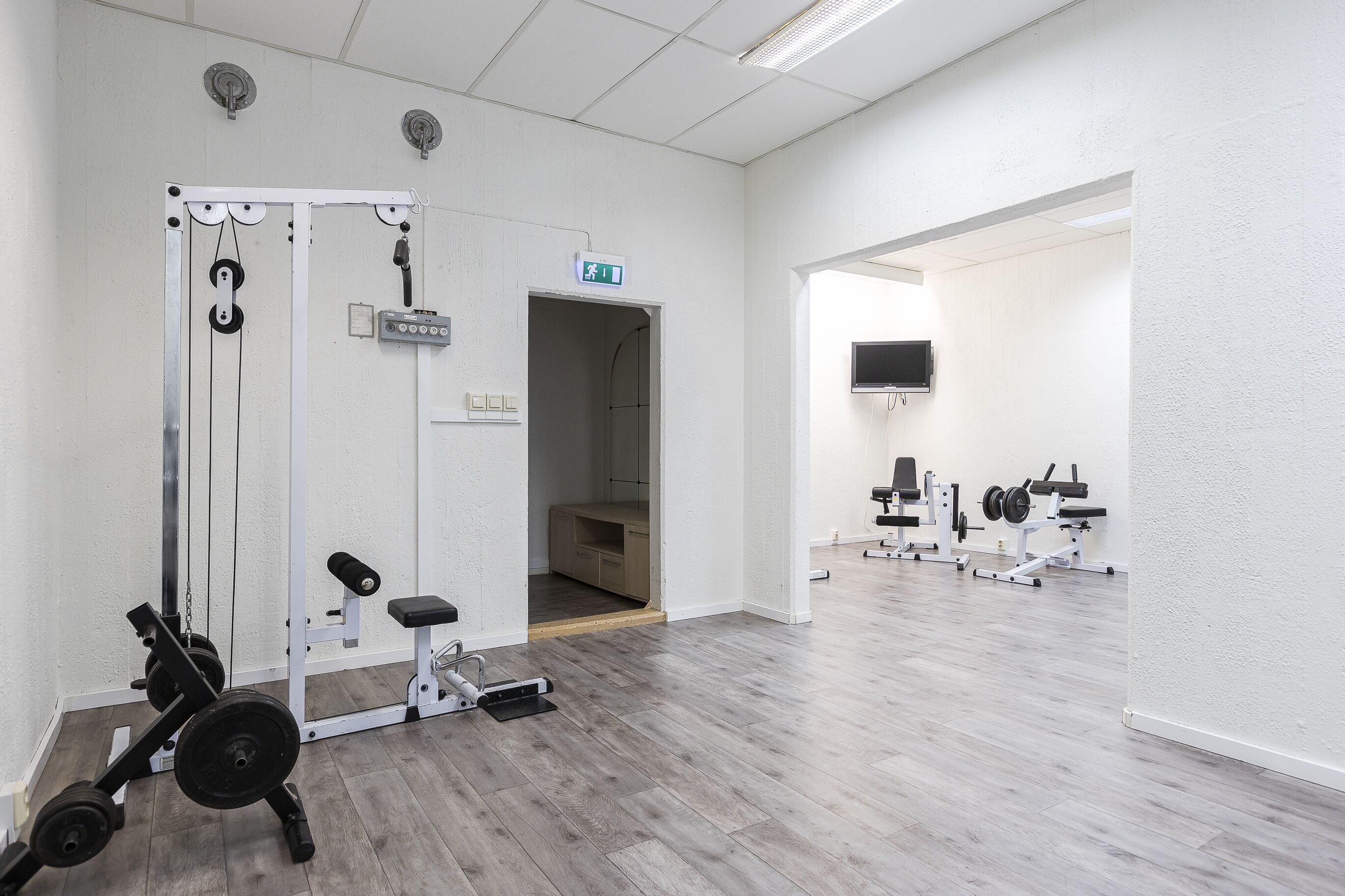 Une salle de sport équipée de matériel d’exercice, avec un miroir et un téléviseur accroché au mur.