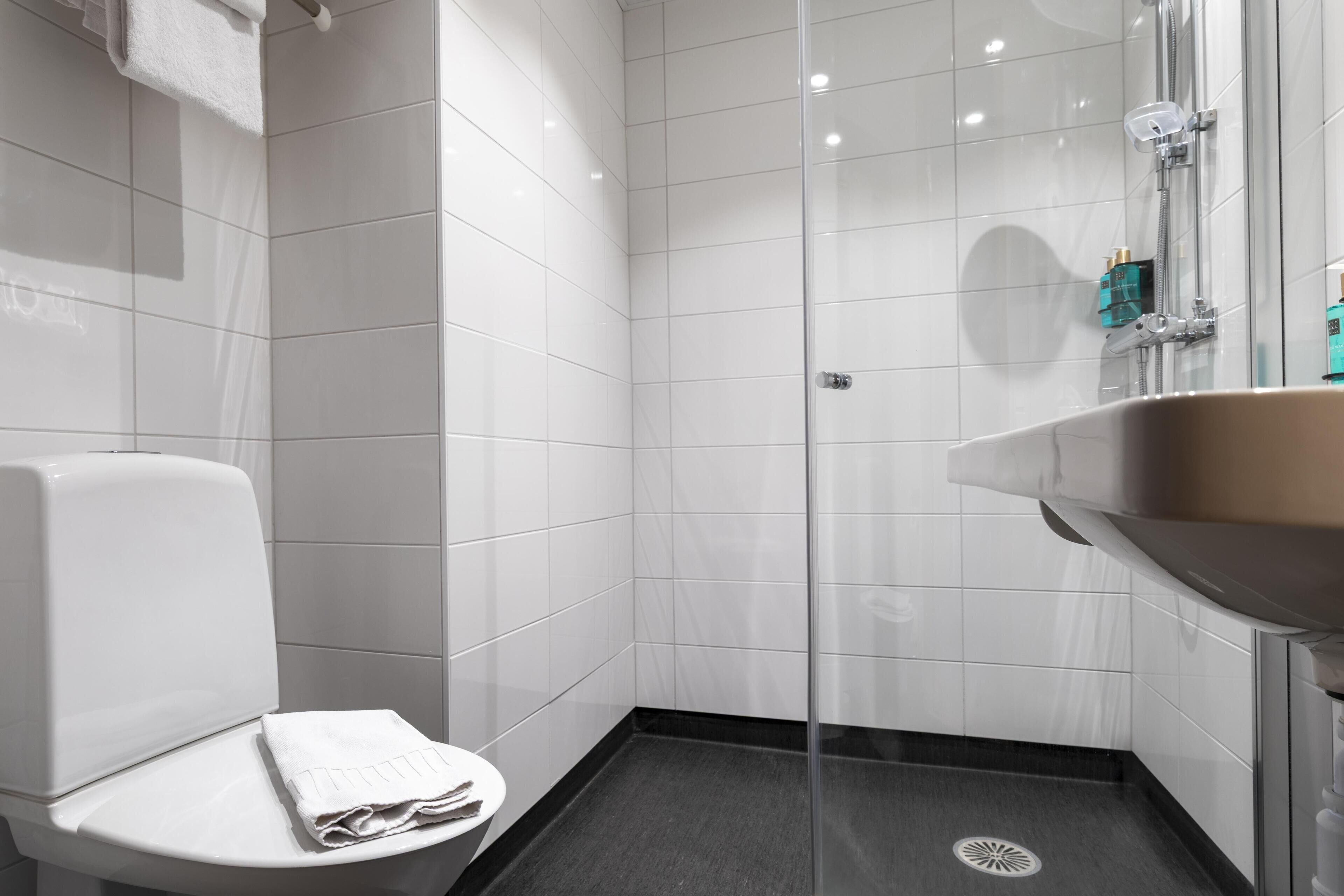 A modern bathroom with white tiles, a glass shower enclosure, a white toilet, and a sink with a mirror.