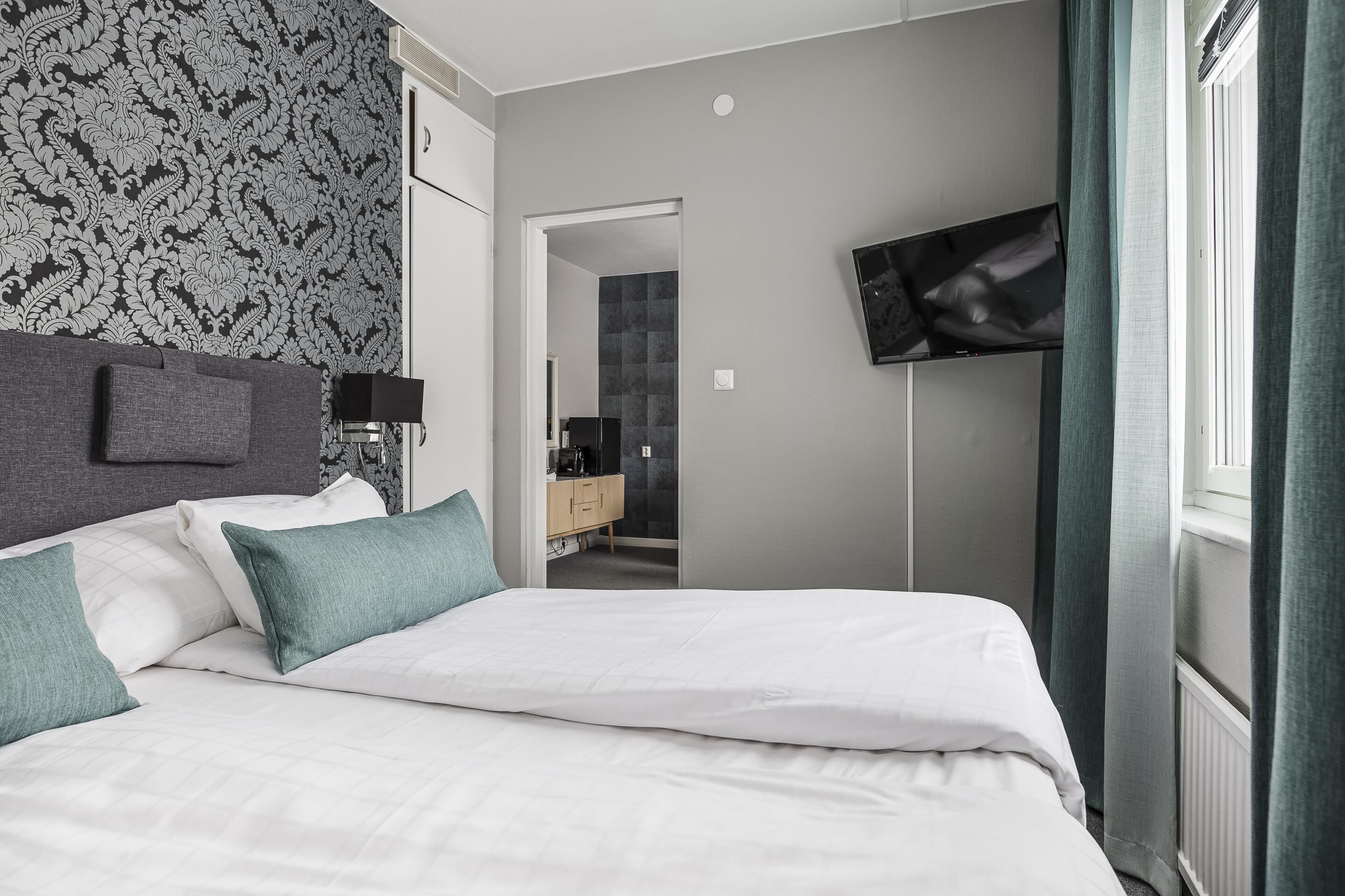 A modern hotel room with a neatly made bed, a flat-screen TV mounted on the wall, and a walk-in closet.