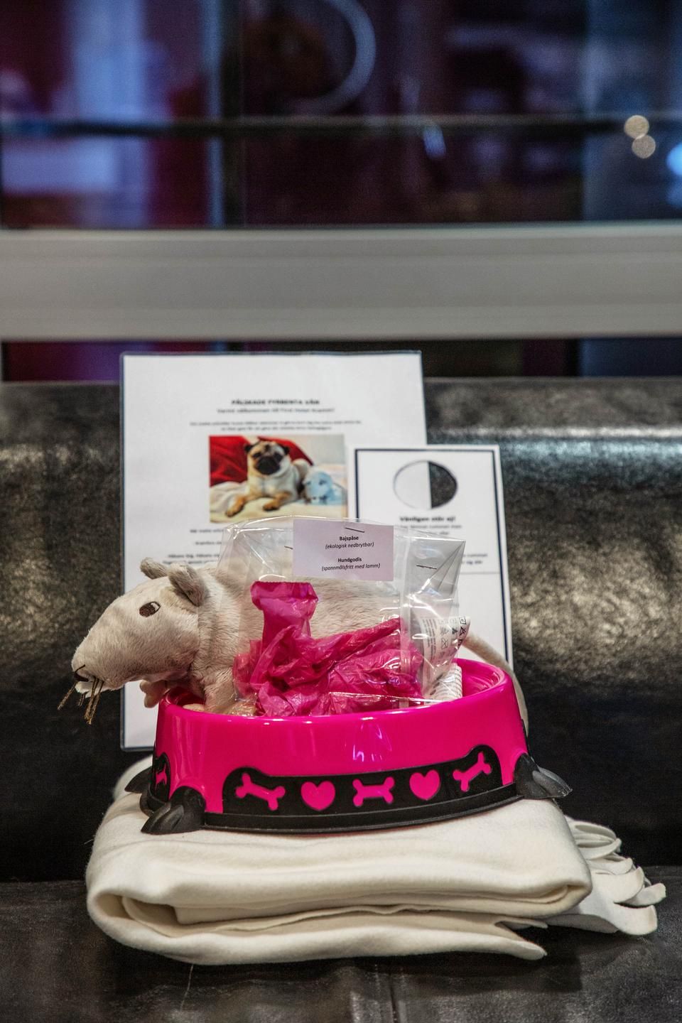 Un peluche en una cesta rosa con una etiqueta, colocado sobre una mesa con una tarjeta de menú al fondo.