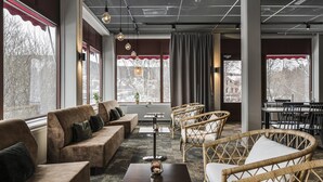 Un espace salon confortable avec des canapés, des fauteuils en osier et une table basse. De grandes fenêtres offrent une vue sur l’extérieur.