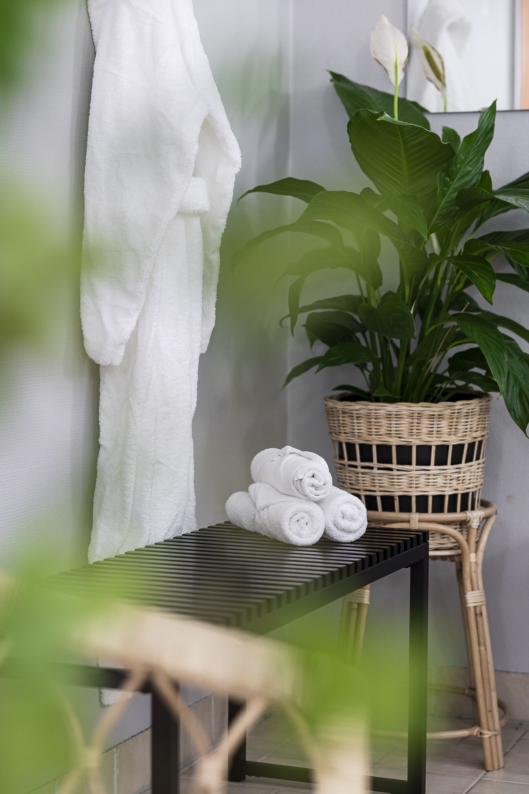 Un baño con una toalla blanca colgada en la pared, una cesta de mimbre con toallas dobladas y una planta en maceta.