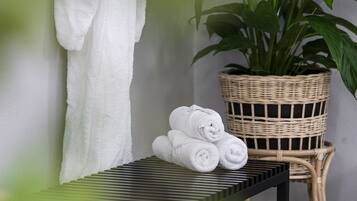 Un baño con una toalla blanca colgada en la pared, una cesta de mimbre con toallas dobladas y una planta en maceta.