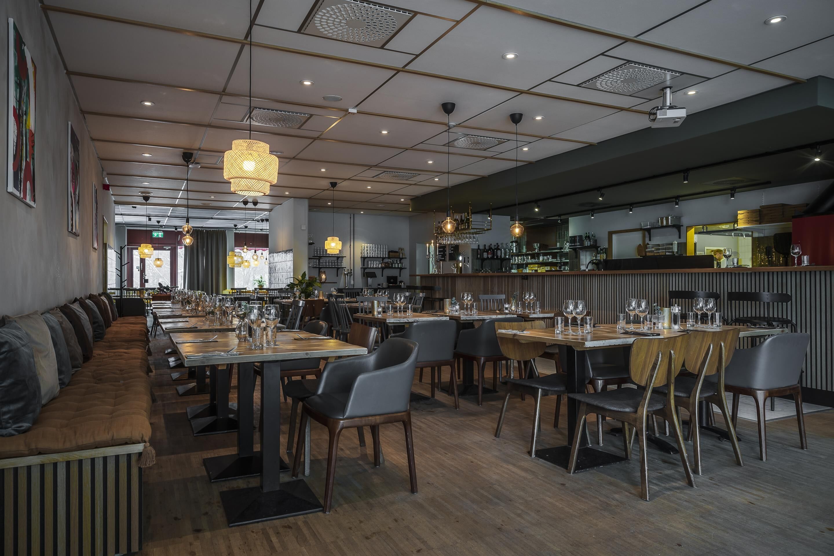 Un restaurante moderno con mesas comunes alargadas, cabinas individuales para comer y una zona de bar.