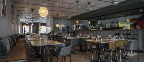 Un restaurante moderno con mesas comunes alargadas, cabinas individuales para comer y una zona de bar.