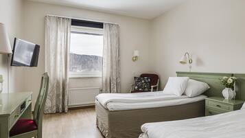 Ett hotellrum med en säng, ett skrivbord, en stol, en tv och ett fönster med gardiner.
