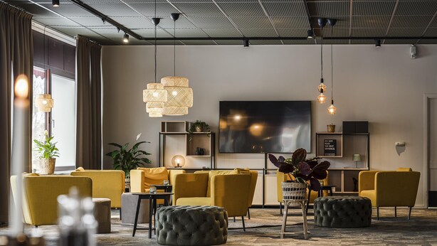 Un salon moderne avec des canapés jaunes, un grand téléviseur à écran plat et des luminaires suspendus.