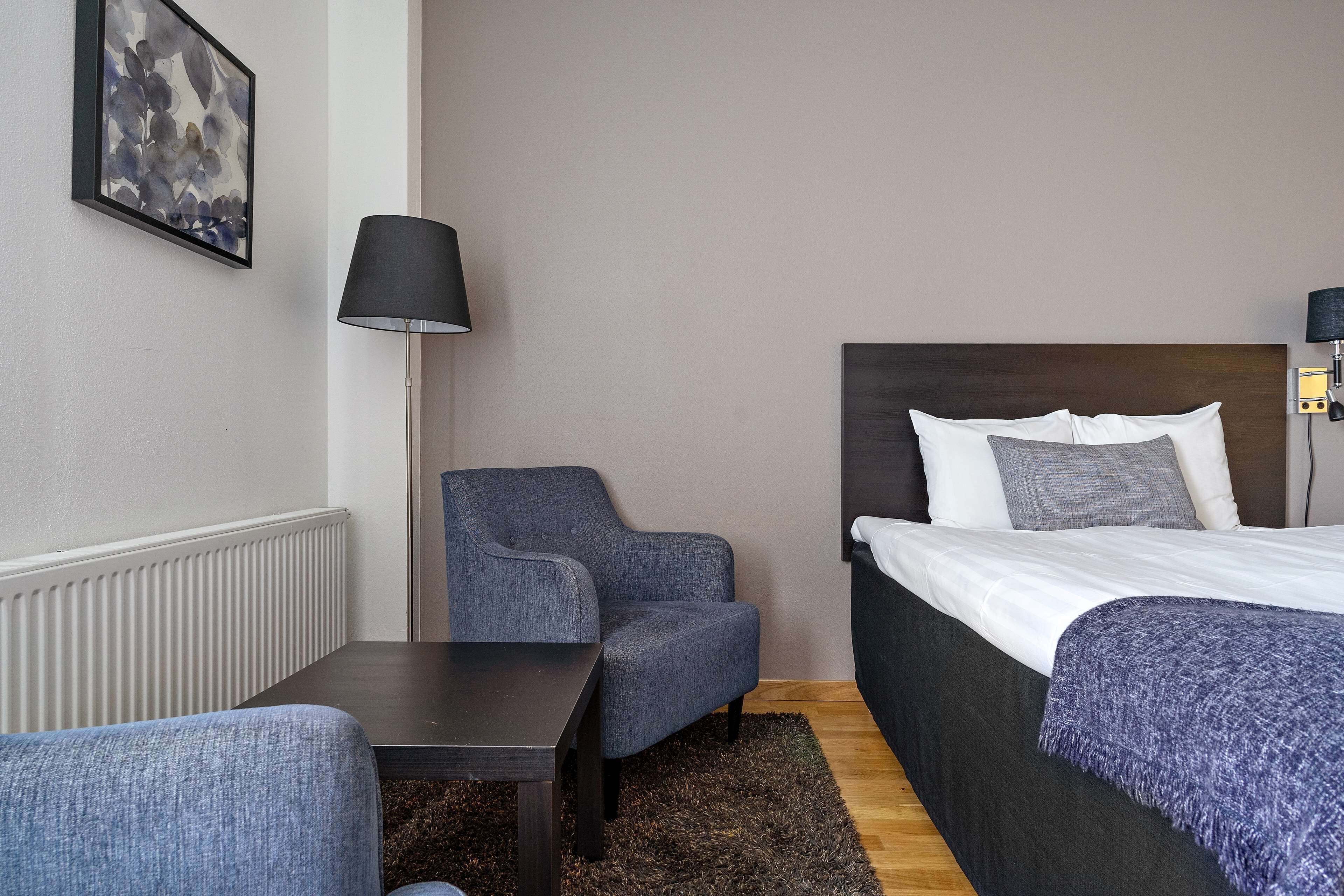 Una habitación de hotel con cama, una silla, una mesa y una lámpara.