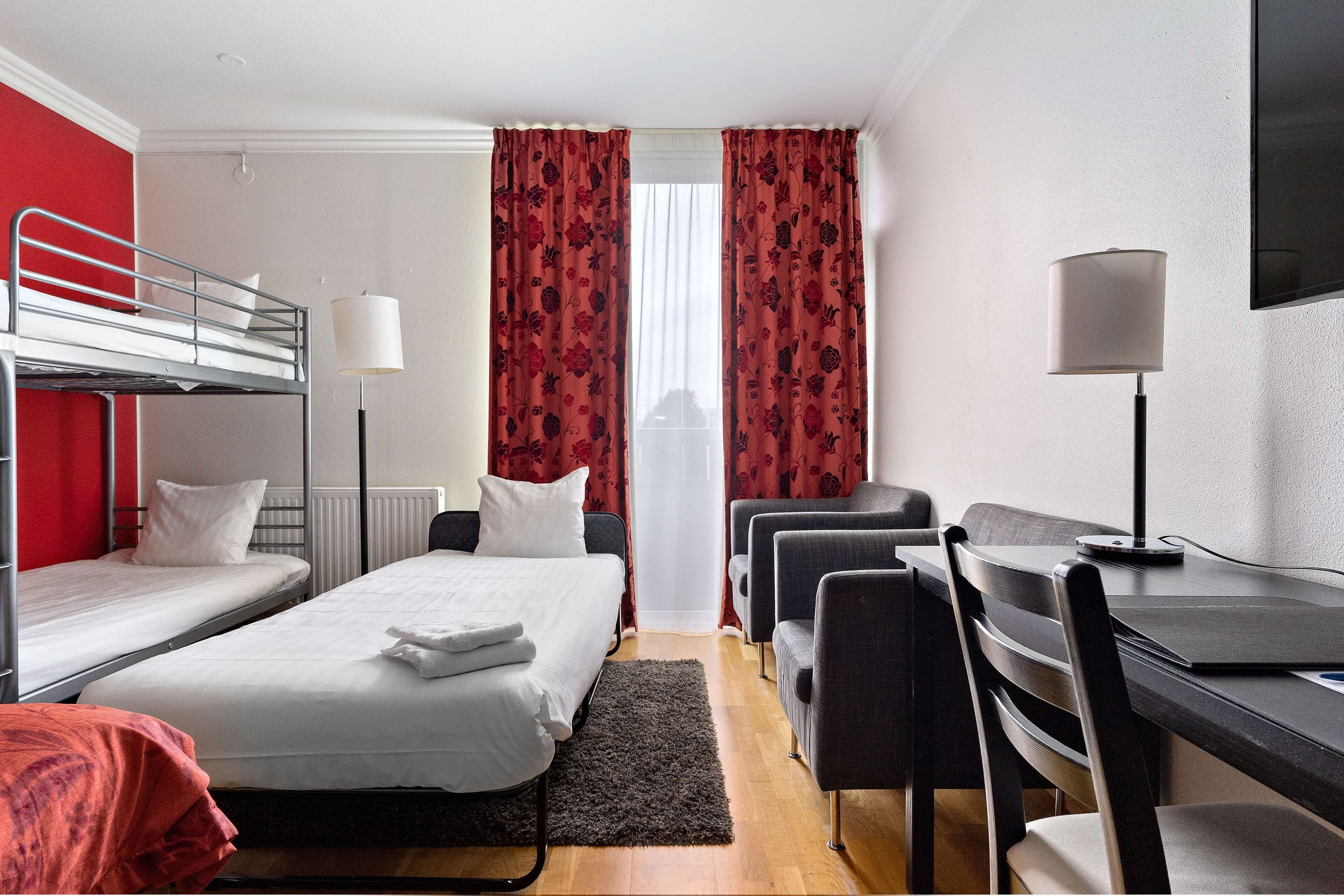 Habitación de hotel con literas, un escritorio con silla, una lámpara y un televisor.