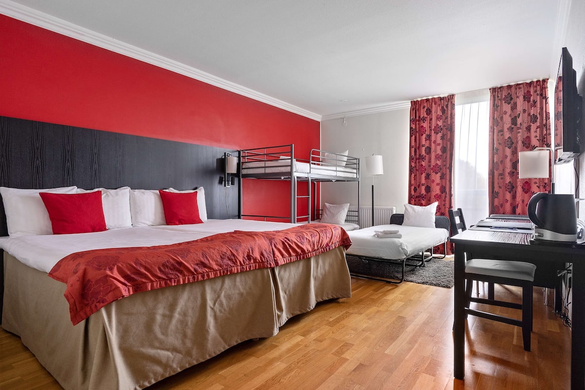 A hotel room with a bunk bed, a desk with a chair, a lamp, and a television.