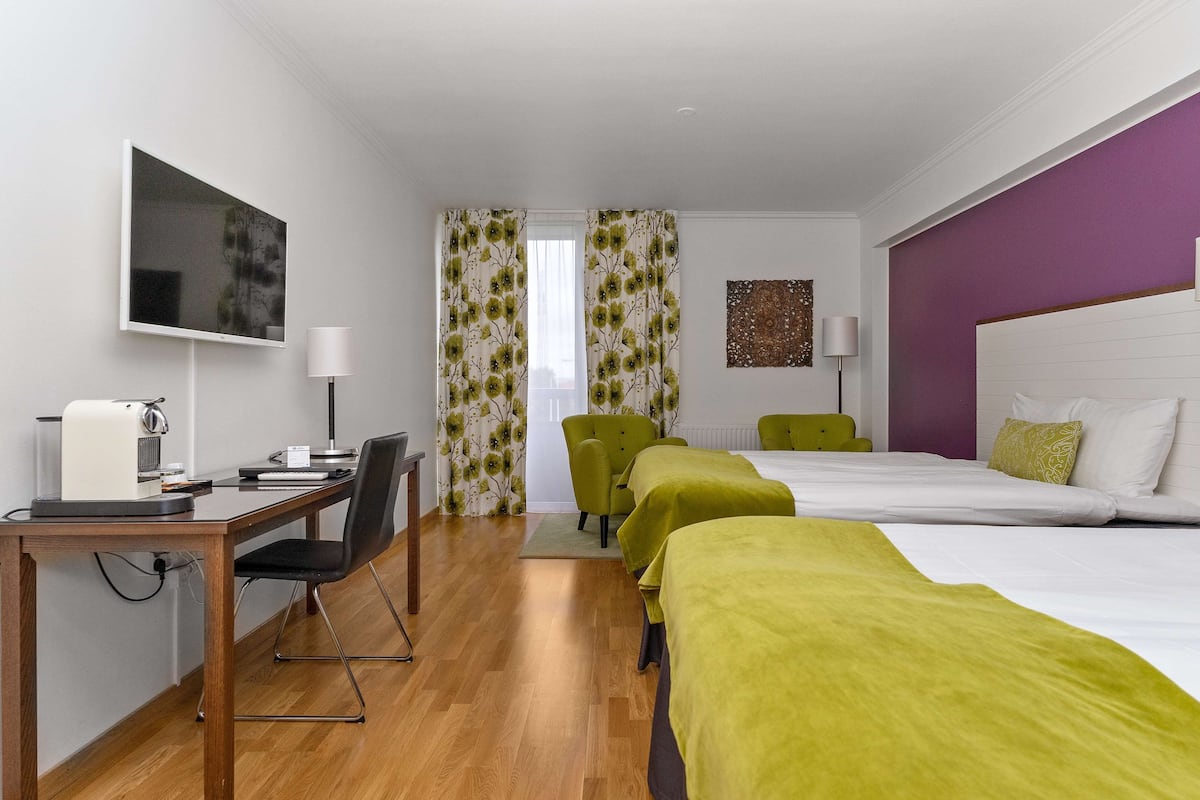 A hotel room with a desk, two beds, a chair, and a TV.
